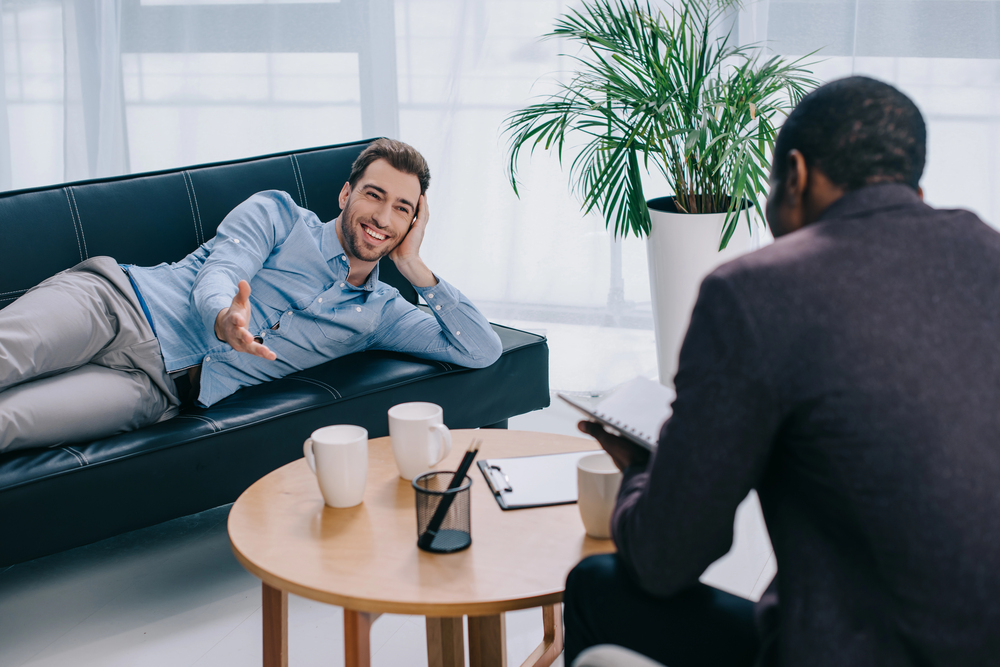 picture of a man in couch holding his head while speaking to a therapist