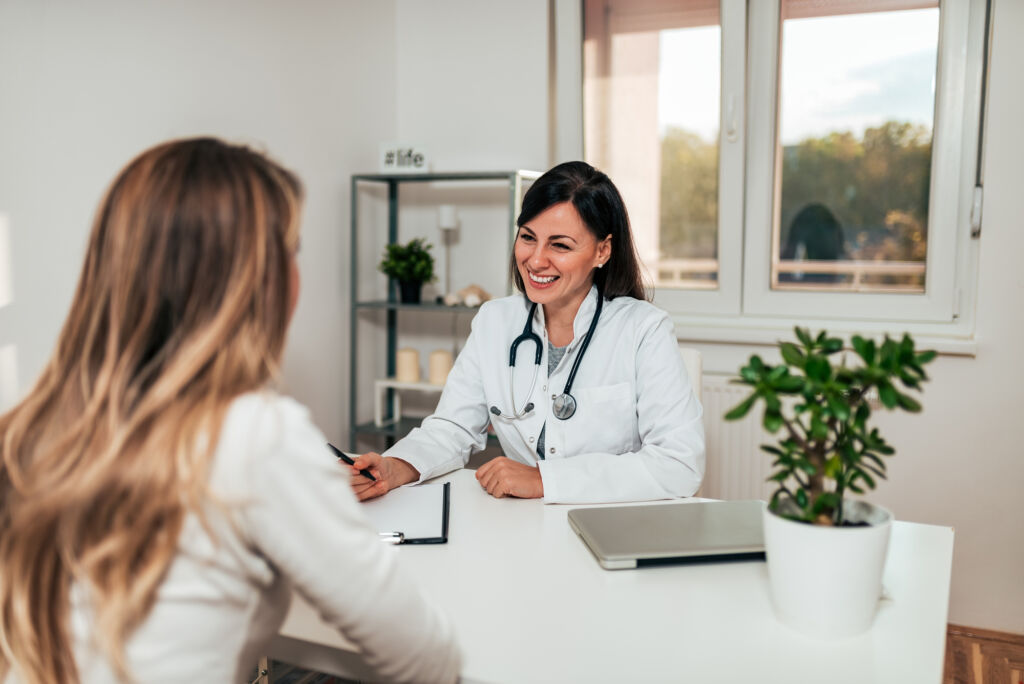 A doctor in a white coat smiles while talking to a patient in an office, discussing medication-assisted treatment